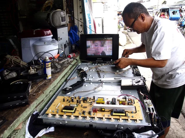 An electronics repair shop technician works on a flat screen tv.
