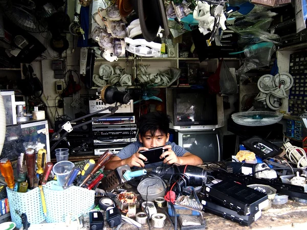 An electronics repair shop technician plays with his cellphone