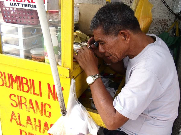 A watch repair man works on a watch in his stall