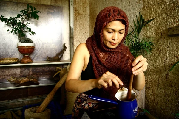 A woman prepares hot cocoa drink manually from freshly ground cocoa beans.