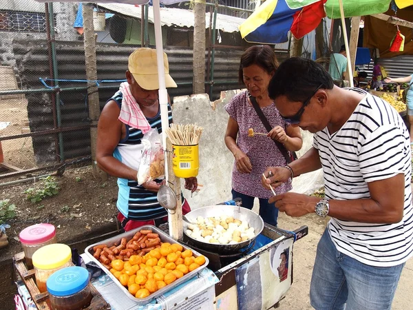 A food vendor cooks fish balls, sausages and quail eggs which he sells on a food cart
