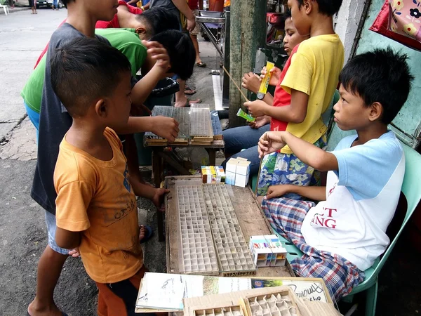 Young children gather in front of a vendor selling spiders used for spider fighting