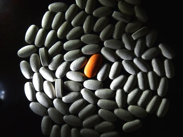 Orange colored pill among white pills