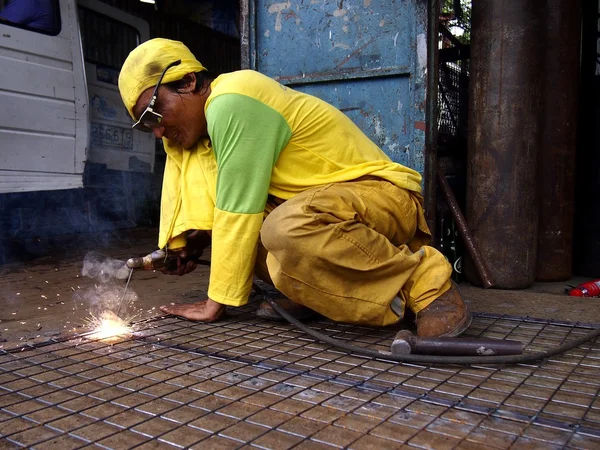 A welder works on a fence in front of a shop.