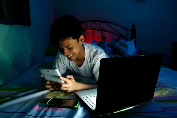 Young Teen in front of a laptop computer and on a bed and using a tablet