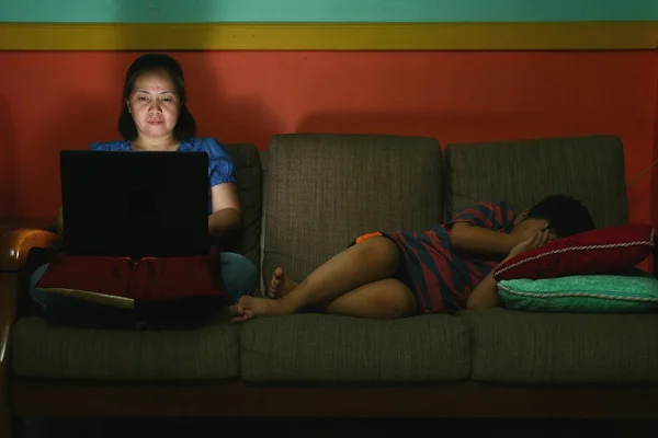 Woman using a laptop computer and a Young kid sleeping on a couch