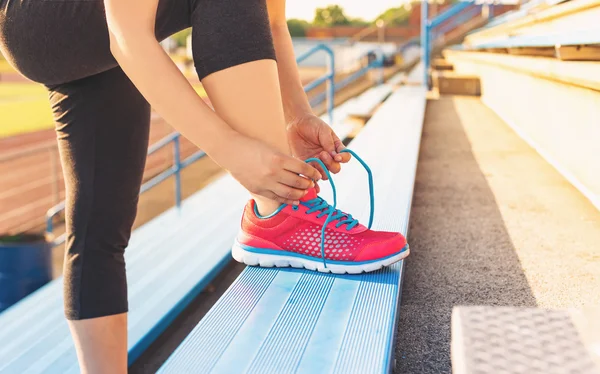 Female jogger tying her shoes on the bleachers
