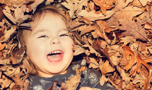 Happy toddler girl smiling while lying down in a pile of leaves