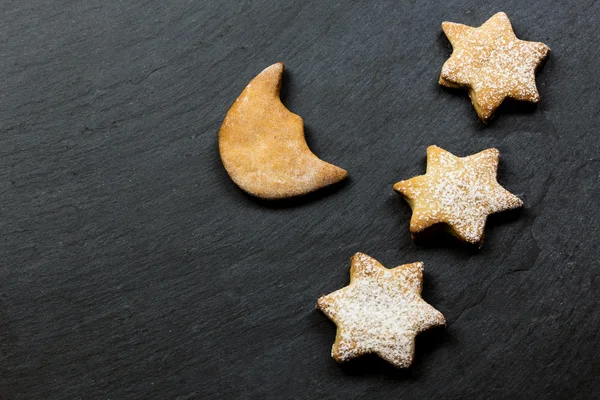 Three stars cookies with moon shape cookie over slate background