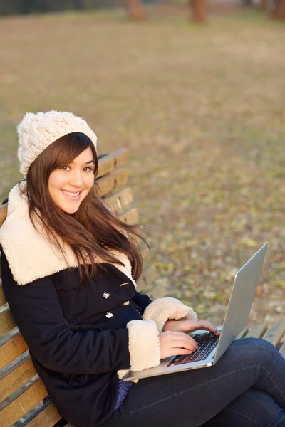 Girl sitting with laptop on bench in park