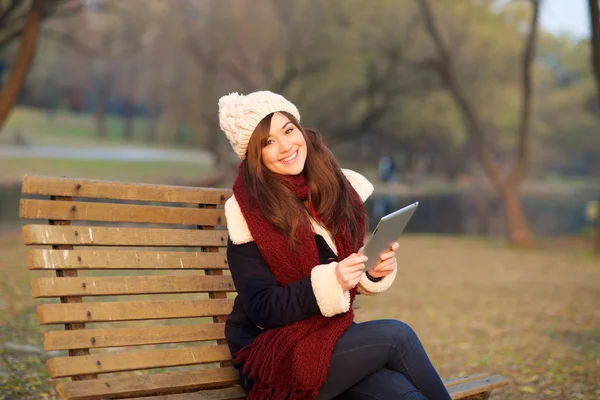Girl sitting with tablet on bench in park