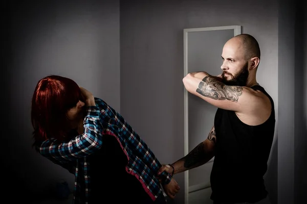 Muscular tattooed man beating his redhead wife.