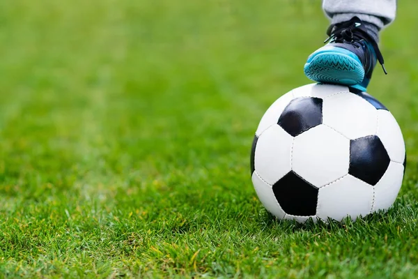 Feet of child on football / soccer ball on grass.