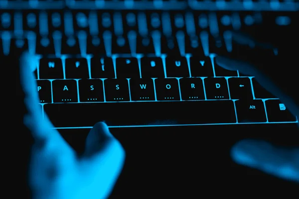 Hacker typing on the illuminated  keyboard by night.