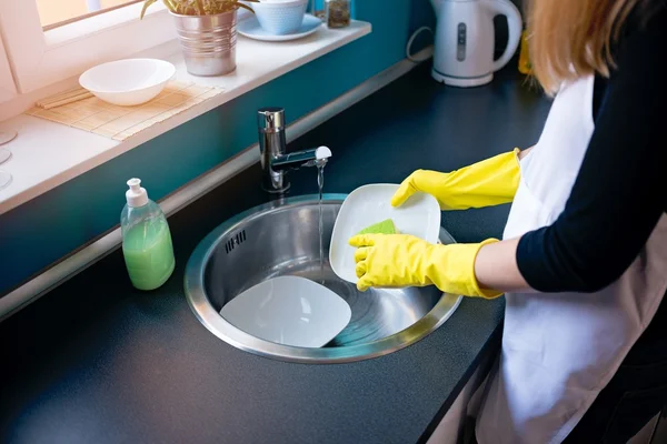 Woman washing dishes in the kitchen with sponge.