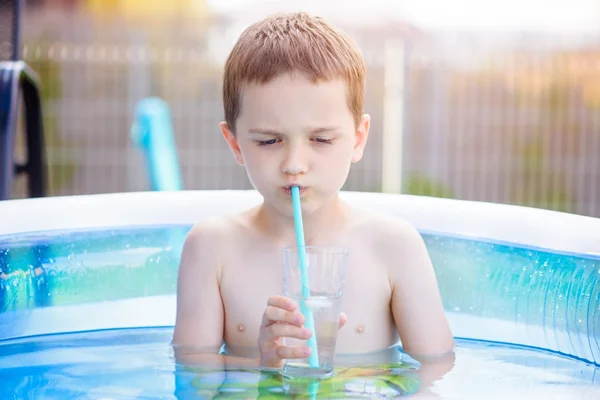 Child drinking lemonade in inflatable garden pool