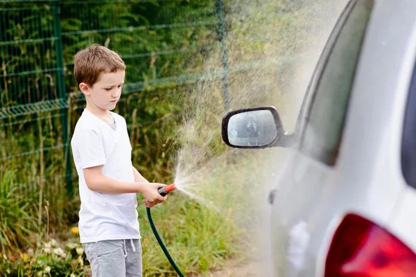 Little boy washing silver car in the garden