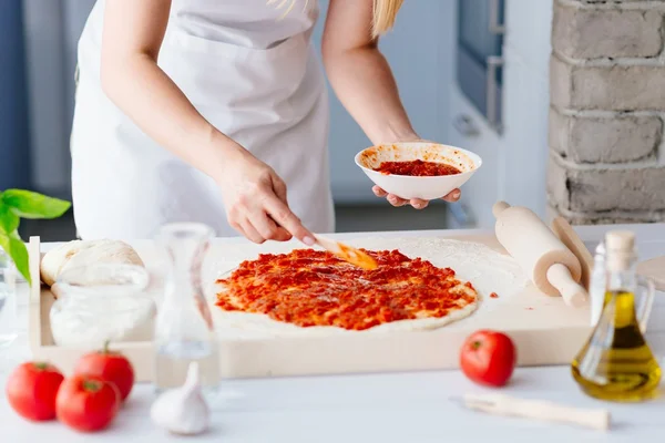 Woman adding tomato sauce on pizza