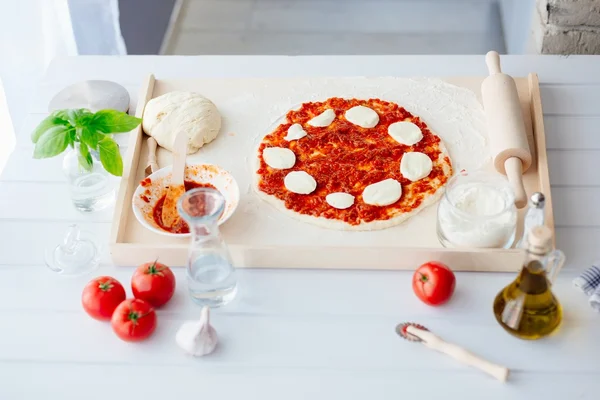 Raw margherita pizza on wooden pastry board