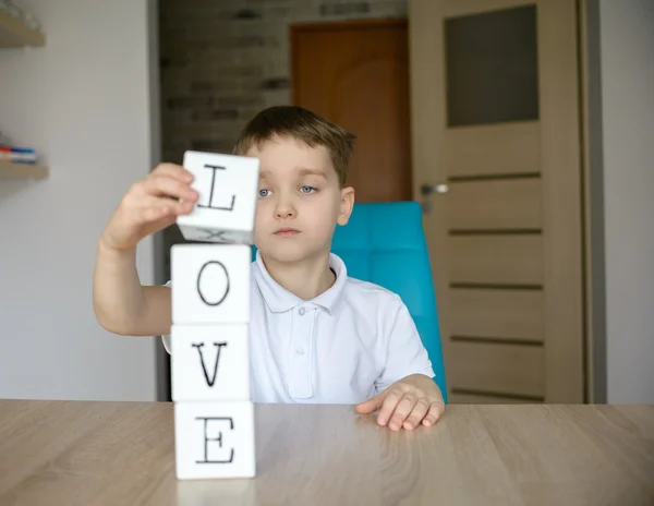 Little boy plays with cubes and puts it together in word \