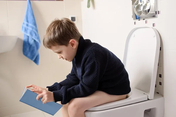 Boy sitting on the toilet and reading a book