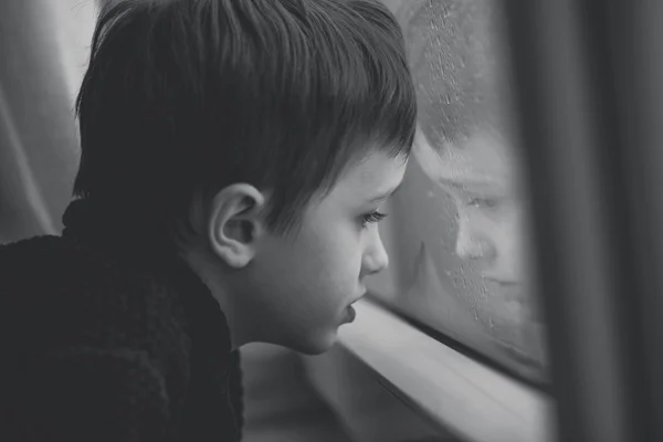 Little boy waiting by window for stop raining - black and white