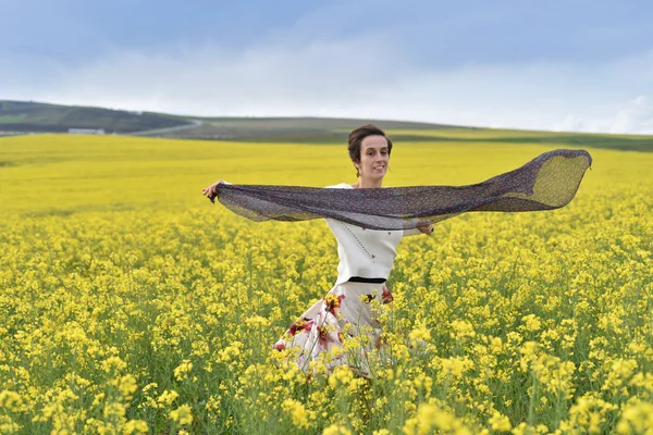 Smiling young woman playing with scarf in a canola field