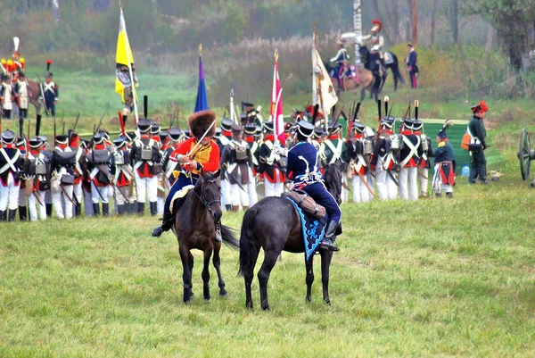 Reenactors dressed as Napoleonic war soldiers ride horses.