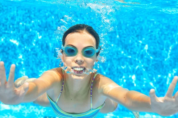 Child swims in pool underwater, funny happy girl in goggles has fun under water and makes bubbles, kid sport on family vacation