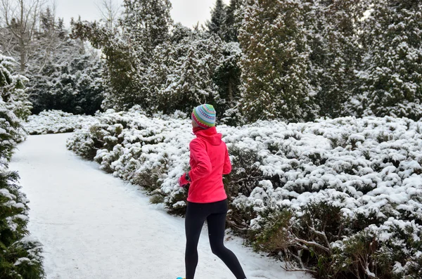 Winter running in park: happy woman runner jogging in snow, outdoor sport and fitness concept