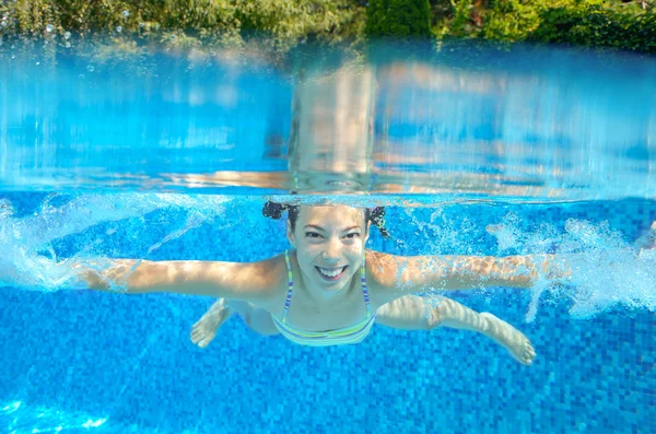 Happy girl swims in pool underwater, active kid swimming