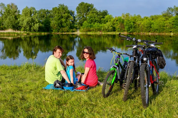 Family bike ride outdoors, active parents and kid cycling and relaxing near beautiful river