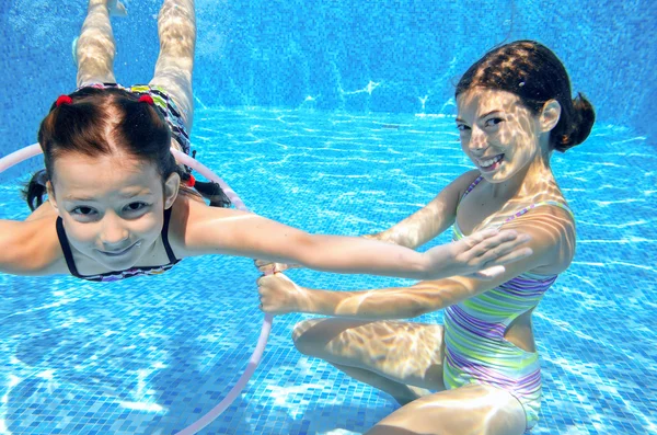 Happy children swim in pool underwater, girls swimming, playing and having fun, kids water sport