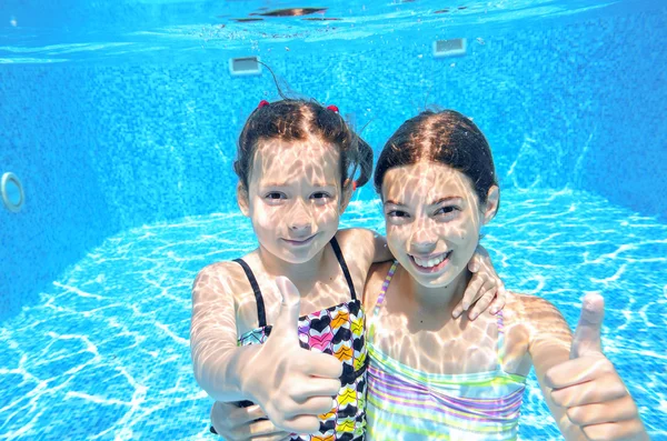 Happy children swim in pool underwater, girls swimming, playing and having fun, kids water sport