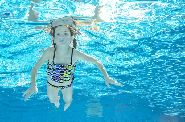 Child swims in pool underwater, happy active girl has fun in water, kid sport on family vacation