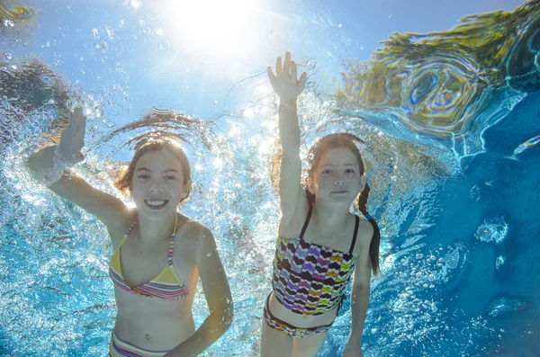 Children swim in pool underwater, happy active girls have fun in water, kids sport on family vacation