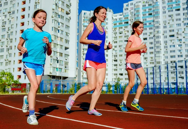 Family sport, happy active mother and kids jogging on track, running and working out on stadium in modern city