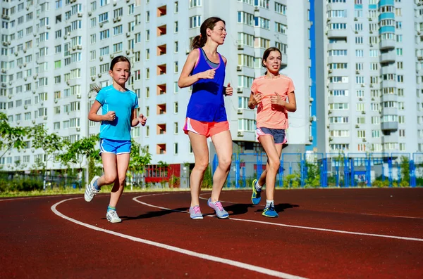 Family sport, happy active mother and kids jogging on track, running and working out on stadium in modern city