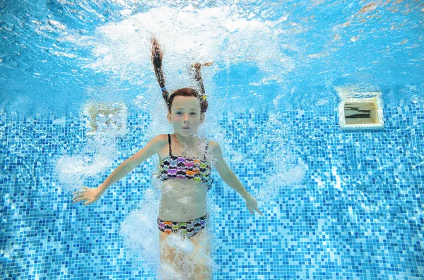 Girl jumps and swims in pool underwater, happy active child has fun in water, kid sport on family vacation