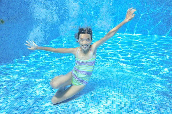 Child swims in pool underwater, happy active girl has fun in water, kid sport on family vacation