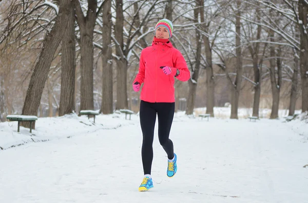 Winter running in park: happy woman runner jogging in snow, outdoor sport and fitness concept