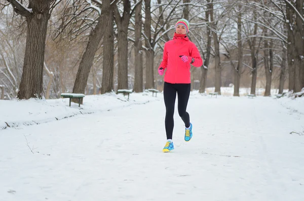 Winter running in park: happy woman runner jogging in snow, outdoor sport and fitness concept
