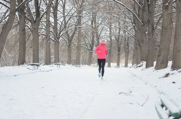 Winter running in park: happy woman runner jogging in snow, outdoor sport and fitness concept