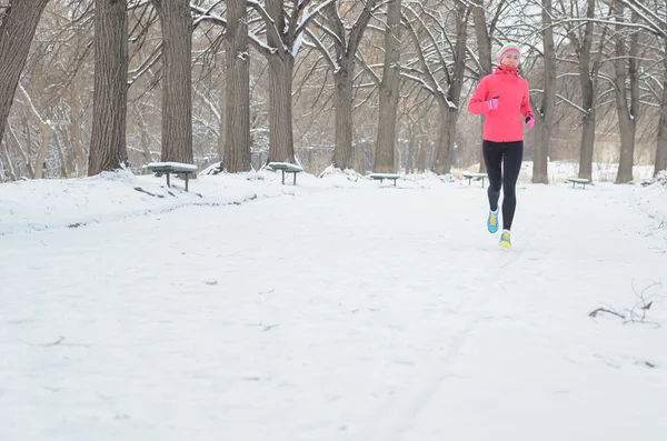 Winter running in park: happy woman runner jogging in snow, outdoor sport and fitness concept