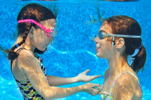 Children swim in pool underwater, happy active girls in goggles have fun under water, kids sport on family vacation