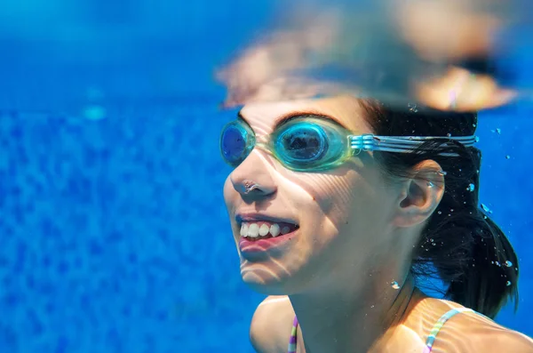 Child swims in pool underwater, happy active girl in goggles has fun under water, kid sport on family vacation