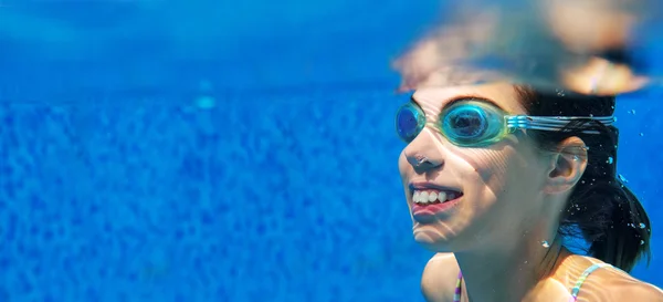 Child swims in pool underwater, happy active girl in goggles has fun in water, kid sport on family vacation