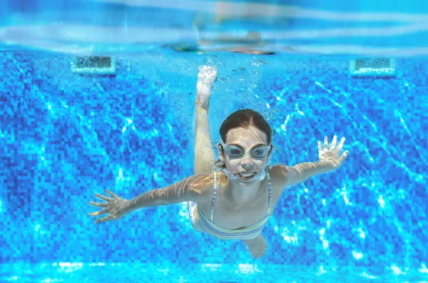 Child swims in pool underwater, happy active girl in goggles has fun under water, kid sport on family vacation