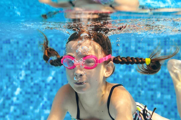 Child swims in pool underwater, happy active girl in goggles has fun under water, kid sport on family vacation