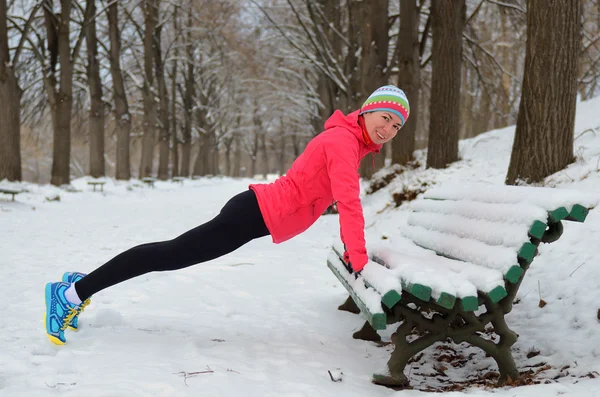 Winter running in park: happy woman runner warming up and exercising before jogging in snow, outdoor sport and fitness concept